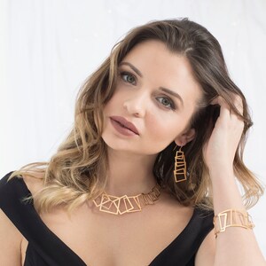 May include: A gold geometric necklace and earrings set with a modern, abstract design. The necklace features a series of interconnected squares and rectangles, while the earrings are long and dangle, with stacked squares.