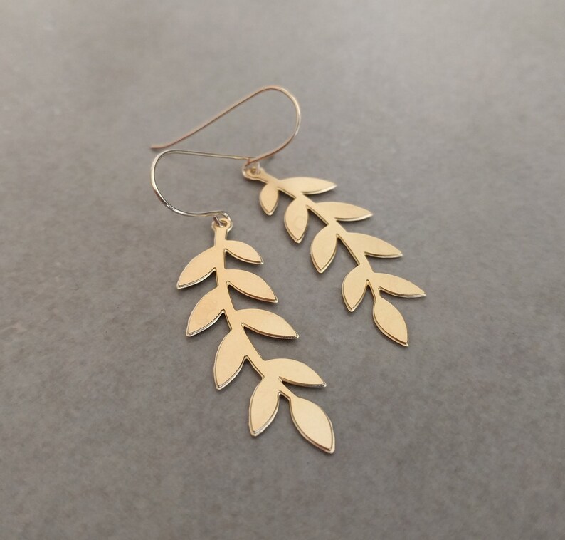May include: A pair of gold leaf earrings with a delicate, branch-like design. Each earring features multiple leaves, creating a flowing and elegant look.