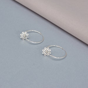 May include: A pair of silver hoop earrings featuring a snowflake design. The earrings are simple and elegant, ideal for everyday wear.