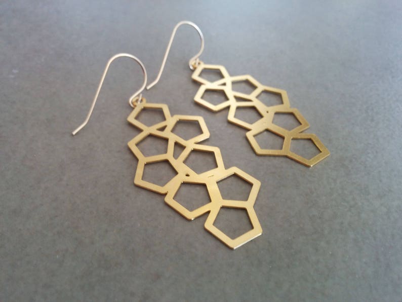 Pu&ograve; includere: Un paio di orecchini geometrici dorati con un design a nido d'ape. Gli orecchini sono in metallo e hanno un motivo delicato e intricato.