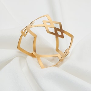 May include: A gold-toned metal bracelet with a geometric design. The bracelet is open and has a square shape with a diamond pattern.