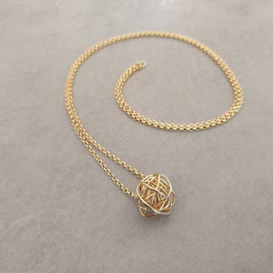 May include: A gold chain necklace with a gold wire sphere pendant.