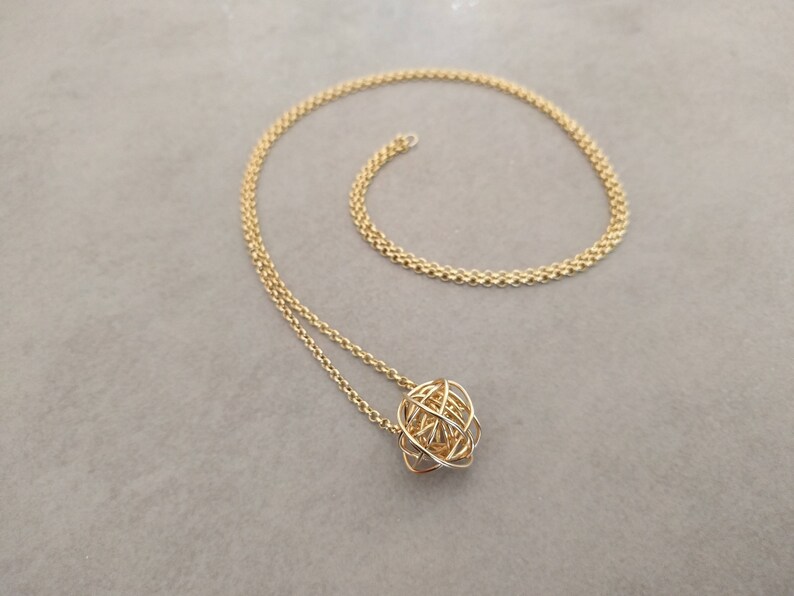 May include: A gold chain necklace with a gold wire sphere pendant.