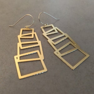May include: A pair of gold-tone geometric earrings with a stacked, layered design. Each earring features multiple rectangular shapes.