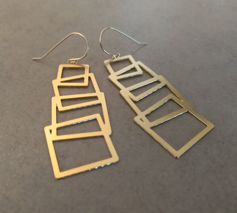 May include: A pair of gold-tone geometric earrings with a stacked, layered design. Each earring features multiple rectangular shapes.
