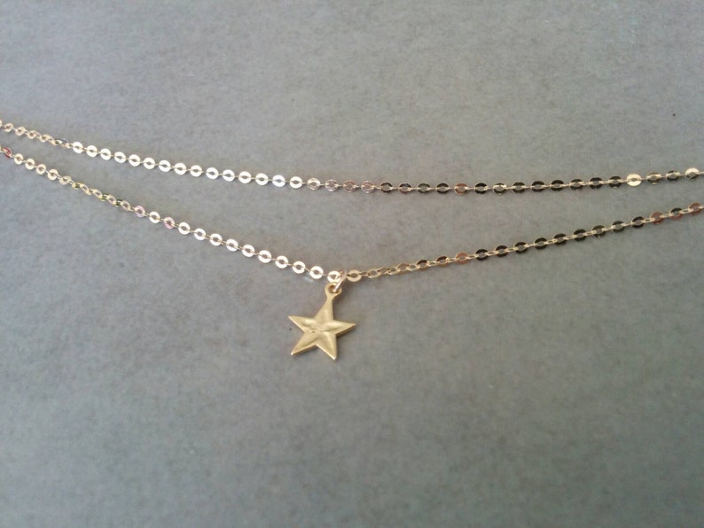 Peut inclure: Un collier d&eacute;licat en cha&icirc;ne dor&eacute;e avec un petit pendentif en forme d'&eacute;toile. La cha&icirc;ne est compos&eacute;e de petits cercles li&eacute;s.