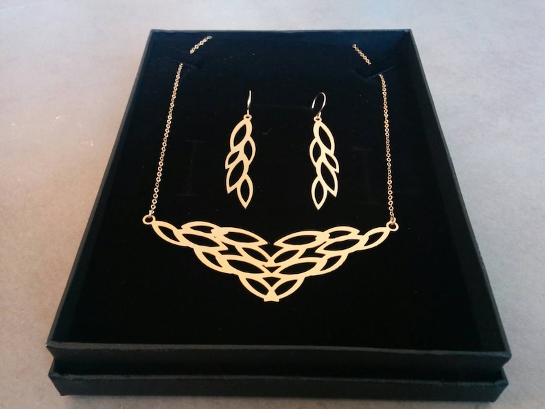 May include: A gold necklace and earrings set with a delicate leaf design. The necklace is a chain with a pendant that features multiple interconnected leaves. The earrings are drop earrings with a similar leaf design.