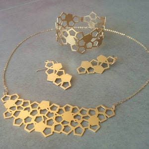 May include: A gold necklace, bracelet, and earrings set with a honeycomb pattern. The necklace and bracelet are made of a delicate chain with a geometric design. The earrings are small and dangle.