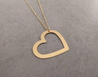 May include: A gold necklace with a large open heart pendant. The heart is made of a single piece of metal and has a smooth, polished finish.