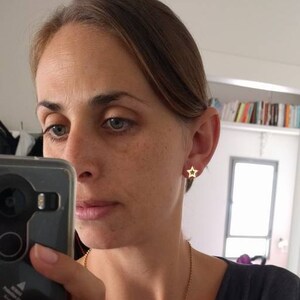 May include: A woman wearing gold star-shaped earrings. The earrings are small and delicate.
