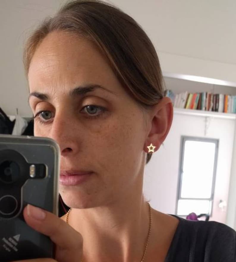 May include: A woman wearing gold star-shaped earrings. The earrings are small and delicate.