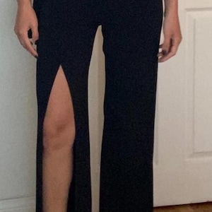 Puede incluir: Pantalones negros de pierna ancha con una larga abertura en la pierna izquierda.