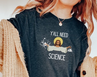 May include: A dark grey t-shirt with the text "Y'all need science" and a cartoon image of Jesus holding an atom and a beaker.