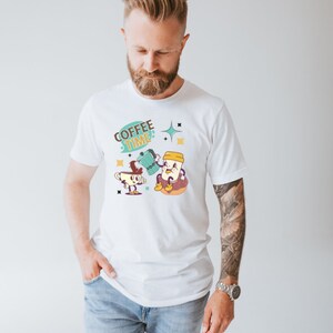 Op de afbeelding: Wit T-shirt met een cartoonillustratie van twee kopjes koffie. De tekst "COFFEE TIME" staat in een spreekballon boven de kopjes.