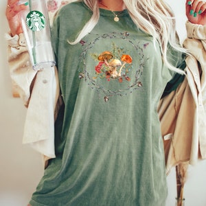 May include: A green oversized t-shirt with a graphic of mushrooms and leaves in a wreath design.
