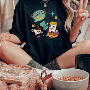 Op de afbeelding: Een zwart T-shirt met een afbeelding van een koffiepot en een koffiekopje met de tekst "COFFEE TIME!" in een retro stijl.