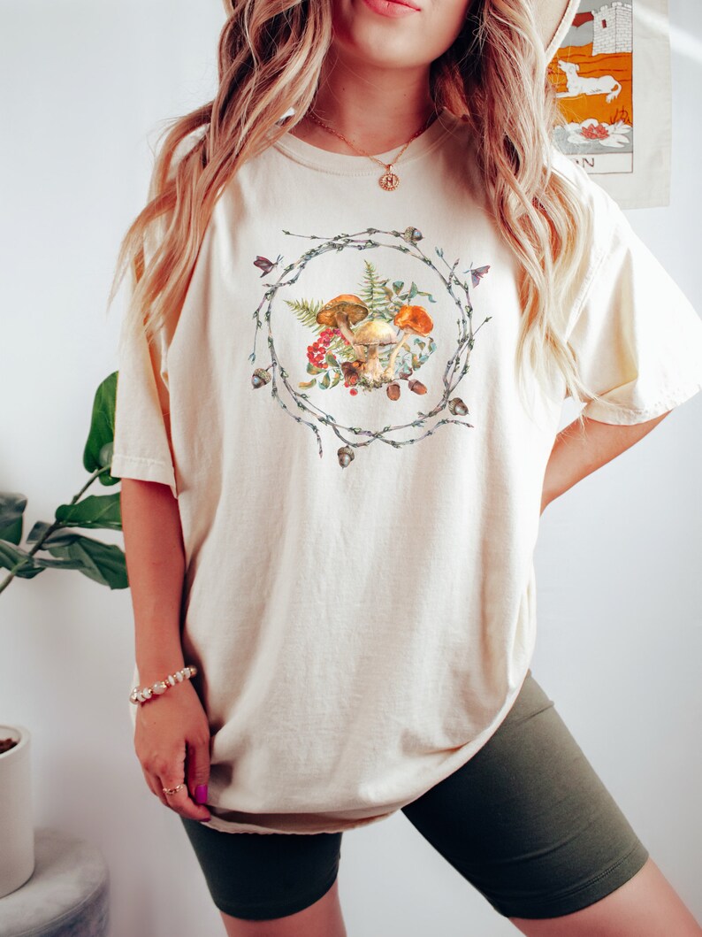 May include: A cream-colored oversized t-shirt with a graphic of mushrooms and greenery in a wreath design.