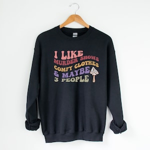 Könnte beinhalten: Schwarzer Pullover mit einem grafischen Aufdruck, der "Ich mag Mordshows, bequeme Kleidung und vielleicht 3 Leute" mit einer Pilzillustration sagt.