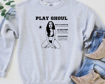 Może przedstawiać: Szara bluza z czarnym nadrukiem graficznym przedstawiającym kobietę w bikini z pająkiem nad nią. Tekst na grafice brzmi "Play Ghoul", "Bride of Frankenstein", "I'm more than just a wife", "20 Questions with Vampira, life, love, and bloodlust", "AAAA00000", "An interview with Lawrence Talbot".