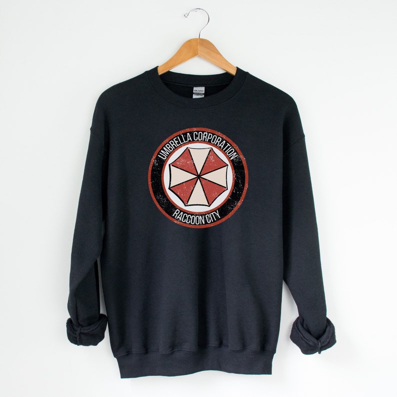 May include: Black sweatshirt with a distressed, circular logo featuring a red and white umbrella with the text "Umbrella Corporation Raccoon City".