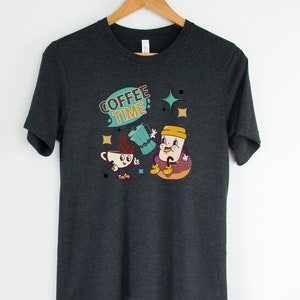 Op de afbeelding: Donkergrijs T-shirt met een afbeelding van een koffiekopje en een donut met de tekst "COFFEE TIME" in een retro stijl.