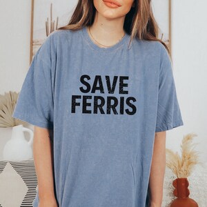 Pode incluir: Uma camiseta azul claro com o texto "SAVE FERRIS" impresso em preto.