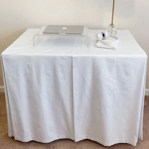 May include: A white table cloth with a white laptop computer on a clear acrylic stand. There are white headphones and a white notebook on the table.