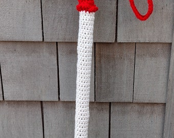 May include: A white crocheted cane cover with a red crocheted top featuring white polka dots. The cane has a black handle and a black tip. A white crocheted strap is attached to the handle.