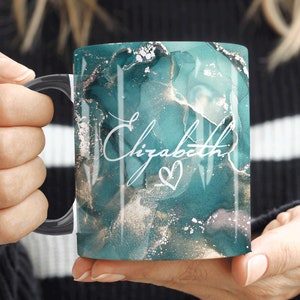 Może przedstawiać: Kubek z marmuru w kolorze turkusowym i złotym z czarnym uchwytem. Na kubku widnieje imię "Elizabeth" napisane białym, ozdobnym pismem z małym serduszkiem.