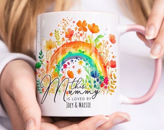 May include: White ceramic mug with a pink handle. The mug features a colorful rainbow with flowers and the text "This Mummy is loved by Joey & Maisie".