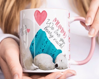Può includere: Una tazza in ceramica bianca con un manico rosa. La tazza presenta un'illustrazione di un orso polare che indossa un maglione blu e turchese con cuori. Il testo sulla tazza recita "Mummy We love you very much!"