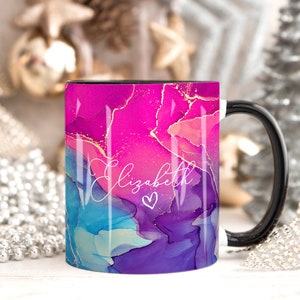 Pu&ograve; includere: Una tazza in ceramica bianca con manico nero. La tazza presenta un design astratto rosa, blu e viola con accenti dorati. Il nome "Elizabeth" &egrave; scritto in corsivo bianco con un piccolo simbolo di cuore.