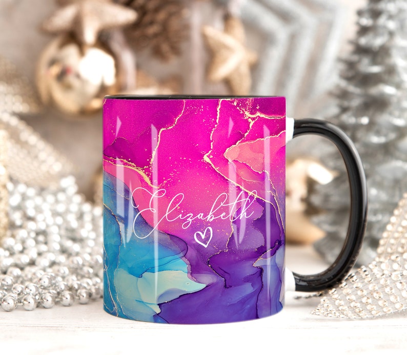 Pu&ograve; includere: Una tazza in ceramica bianca con manico nero. La tazza presenta un design astratto rosa, blu e viola con accenti dorati. Il nome "Elizabeth" &egrave; scritto in corsivo bianco con un piccolo simbolo di cuore.