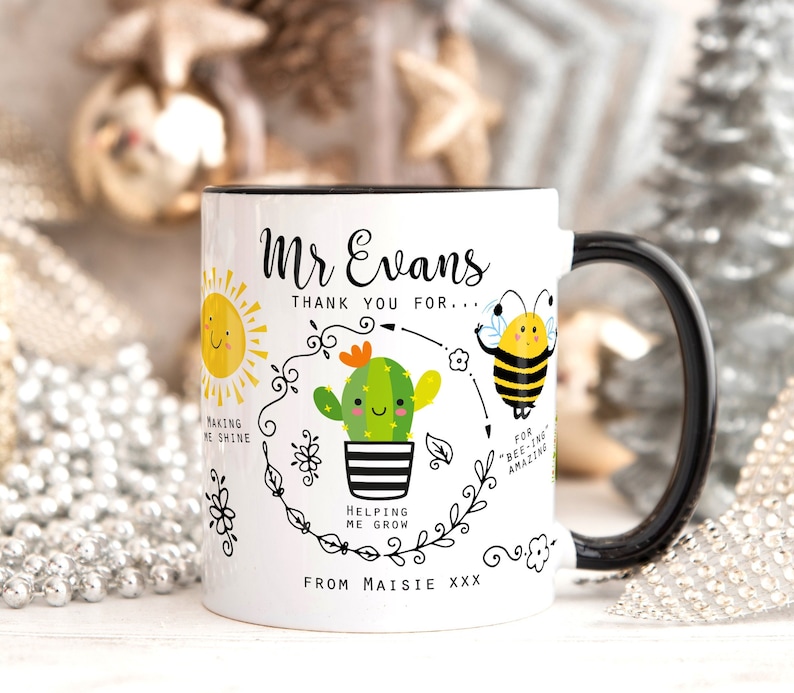 May include: White ceramic mug with a black rim and handle. The mug features a black and white illustration of a sun, a cactus, and a bee. The text "Mr Evans Thank you for... Making me shine Helping me grow For 'bee-ing' amazing From Maisie xxx" is printed on the mug.