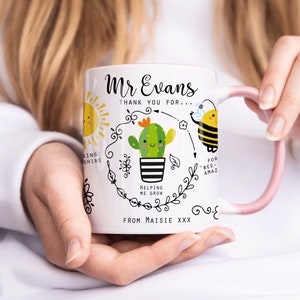 May include: White ceramic mug with a pink handle. The mug has a black and white illustration of a cactus with a smiling face, a sun, and a bee. The text on the mug reads "Mr Evans Thank you for... Helping me grow... For "bee-amaz" From Maisie XXX".