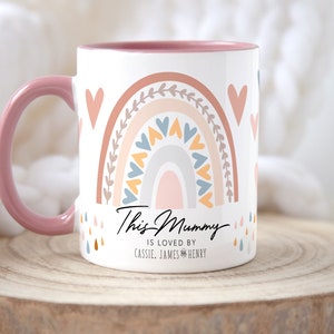 May include: Pink and white ceramic mug with a rainbow design and the text "This Mummy is loved by Cassie, James & Henry".
