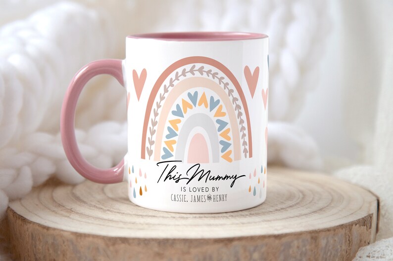 May include: Pink and white ceramic mug with a rainbow design and the text "This Mummy is loved by Cassie, James & Henry".