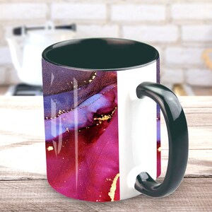May include: A white ceramic mug with a black handle and rim. The mug features an abstract design with shades of purple, pink, and gold.