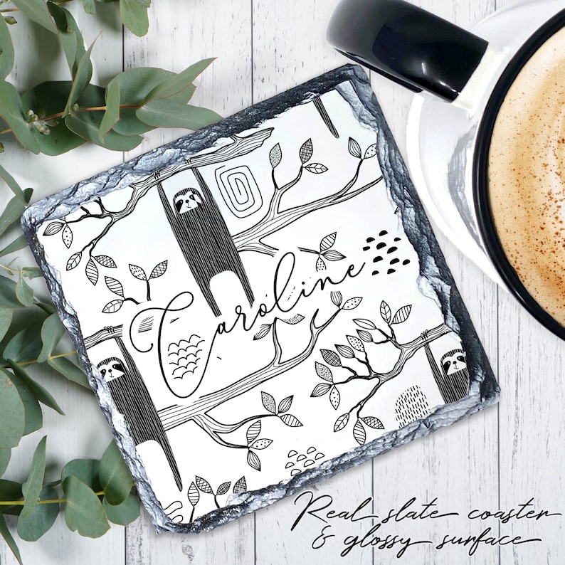 May include: Black and white illustrated coaster featuring sloths hanging from trees with the name "Caroline" written in cursive. The coaster is made of real slate with a glossy surface.