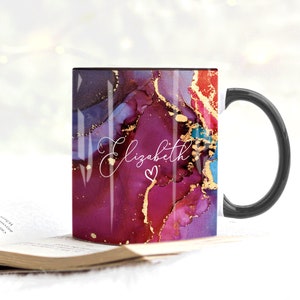 May include: A black coffee mug with a white handle. The mug has a colorful abstract design with gold accents and the name "Elizabeth" written in white script with a pink heart.