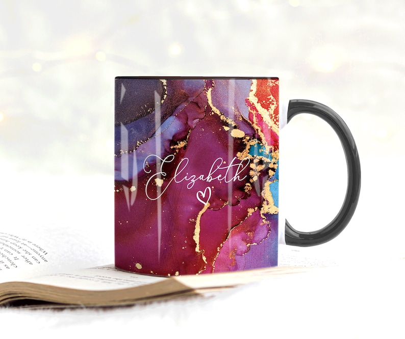 May include: A black coffee mug with a white handle. The mug has a colorful abstract design with gold accents and the name "Elizabeth" written in white script with a pink heart.