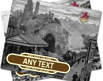May include: A black and white photograph of a train station with a steam engine train pulling into the station. The station is in front of a hill with a castle ruin on top. The train station sign reads "ANY TEXT / BLANK ANY TEXT ANY TEXT / BLANK".