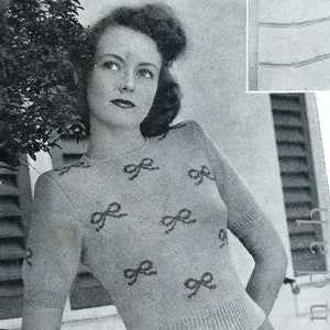 May include: A woman wearing a grey knitted jumper with a bow pattern. The jumper has short sleeves and a crew neck.