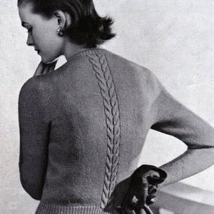 May include: A black and white photograph of a woman wearing a knitted jumper with a cable knit design down the back. The jumper is a light grey colour and has long sleeves. The woman is wearing her hair pulled back and has a simple earring in her left ear. The photo is from a vintage knitting pattern book and includes the text "Patons & Baldwins" in a small rectangle at the top right corner.