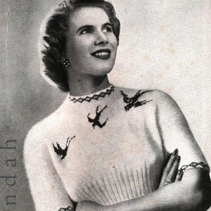 May include: A white knitted sweater with short sleeves and a crew neck. The sweater has a diamond pattern around the neck and three black bird silhouettes on the front.