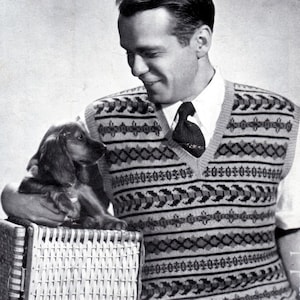May include: A black and white photograph of a man wearing a patterned knitted waistcoat with a dog sitting on a wicker basket. The waistcoat has a V-neck and a geometric pattern in black, white, and grey.