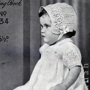 Könnte beinhalten: Ein Schwarzweißfoto eines Babys, das ein weißes Häkelkleid und eine Häkelmütze trägt. Das Baby sitzt auf einer strukturierten Oberfläche. Das Foto stammt aus einem alten Strickmusterbuch.