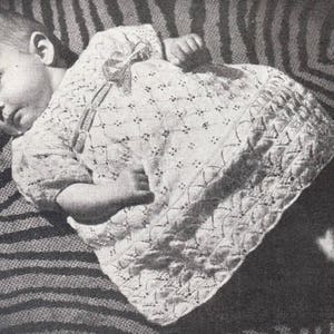 Puede incluir: Una foto en blanco y negro de un bebé que lleva un vestido blanco de ganchillo con un lazo en el hombro. El bebé está acostado sobre una manta a rayas.