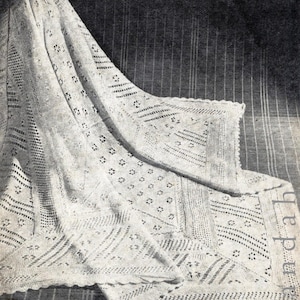 Puede incluir: Una manta de bebé de ganchillo blanco con un delicado patrón de encaje. La manta está doblada y drapeada sobre una superficie. El texto "Lincoln Mills Model No. 1871" es visible en la parte inferior de la imagen.