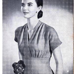 May include: A black and white photo of a woman wearing a knitted sweater with a V-neck and short sleeves. The sweater has a fitted waist and a textured knit.